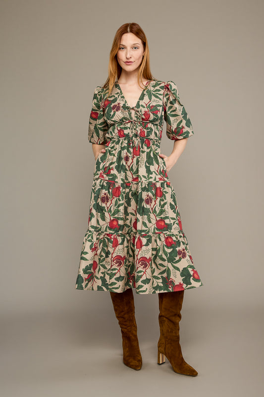A woman modeling a knee-length floral dress with puff sleeves and a smocked waist, paired with brown knee-high boots, against a plain taupe studio background.